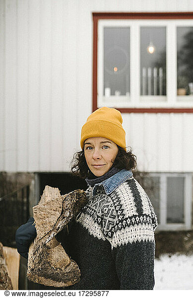 Portrait of mature woman carrying firewood during winter