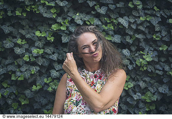 Portrait of mature woman standing in front of wall overgrown with ivy pouting mouth