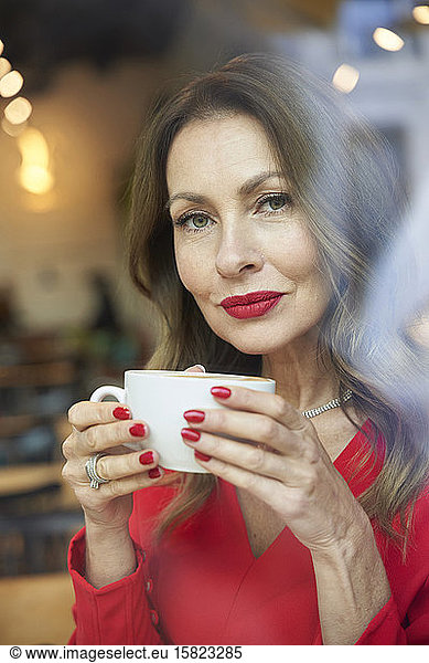 Portrait of mature woman with cup of coffee behind windowpane