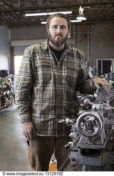 Portrait of mechanic standing by machinery at auto repair shop