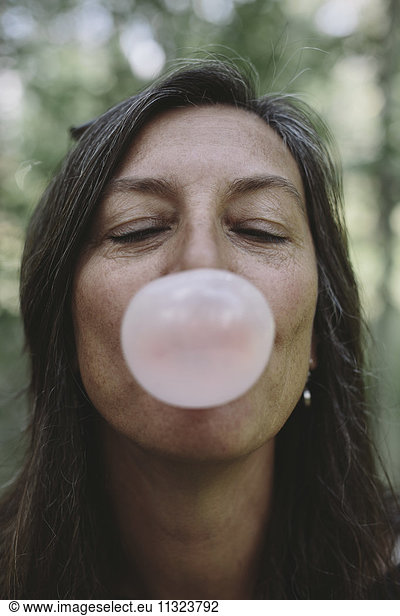 Portrait of middle aged woman blowing bubble gum bubble