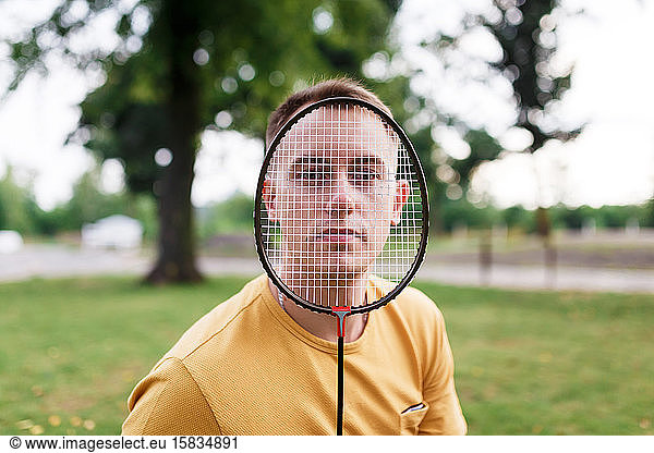 Portrait of millennial man looking through badminton racket at the park