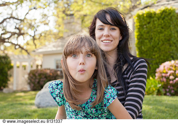 Portrait of mother and daughter pulling face in garden