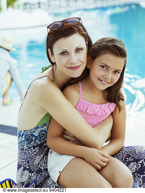 Portrait of mother and daughter sitting by swimming pool