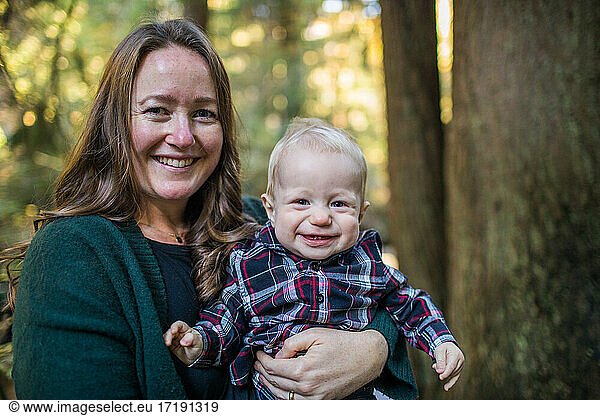 Portrait of mother and young son smiling in forest setting.