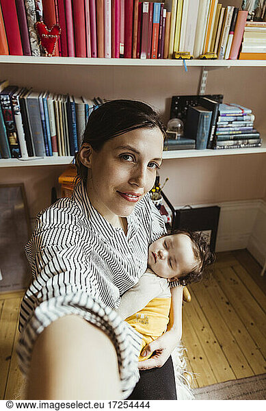 Portrait of mother carrying baby boy while taking selfie at home