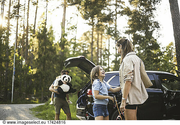 Portrait of mother father and two daughters standing by car at electric vehicle charging station