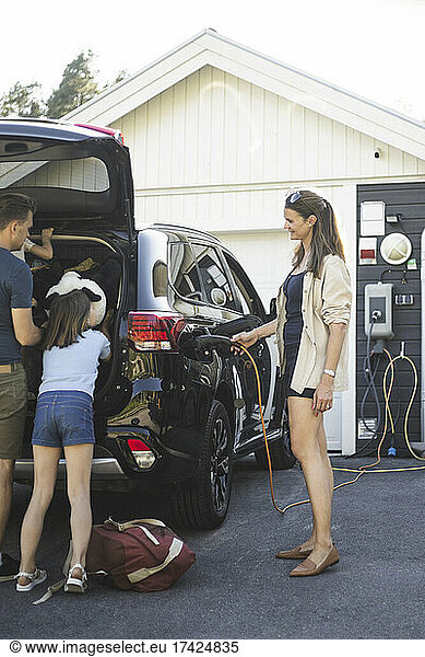 Portrait of mother  father and two daughters standing by car at electric vehicle charging station