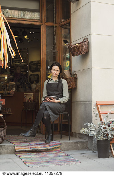 Portrait of owner holding digital tablet sitting at store entrance