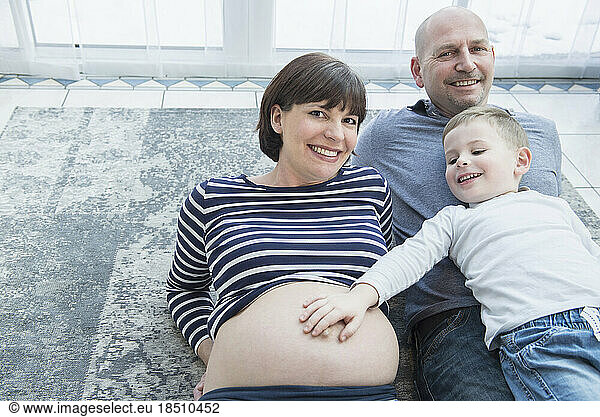 Portrait of parents lying on carpet with son touching mother's belly