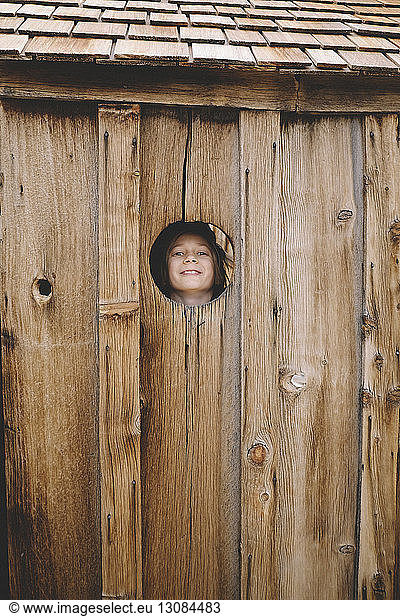Portrait of playful boy seen though wooden wall's hole