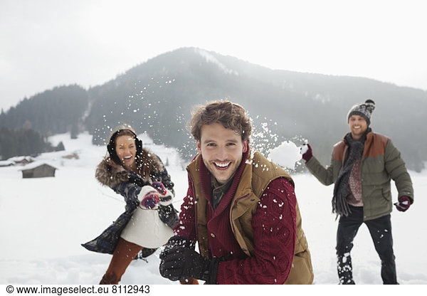 Portrait of playful friends throwing snowballs in field