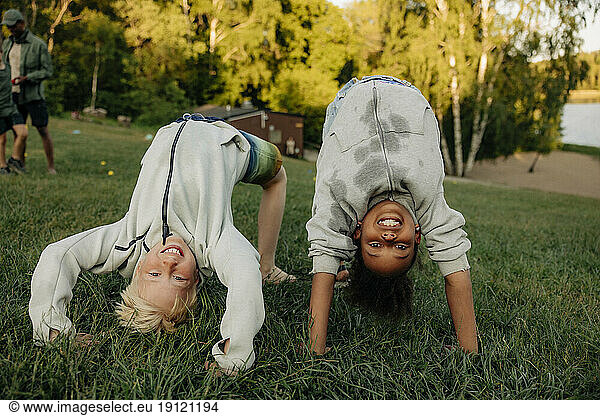 Portrait of playful male and female friends doing bridge position on grass in playground