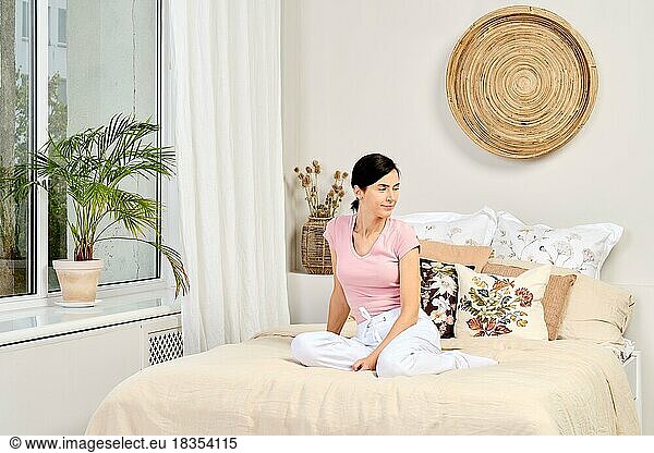 Portrait of pretty woman in casual clothes sitting on bed at home