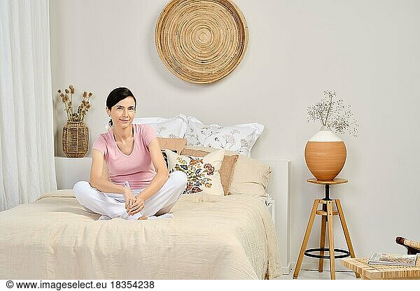 Portrait of pretty woman in casual clothes sitting on bed at home