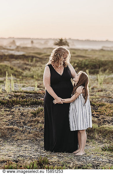 Portrait of redhead mother hugging young daughter at sunset at beach