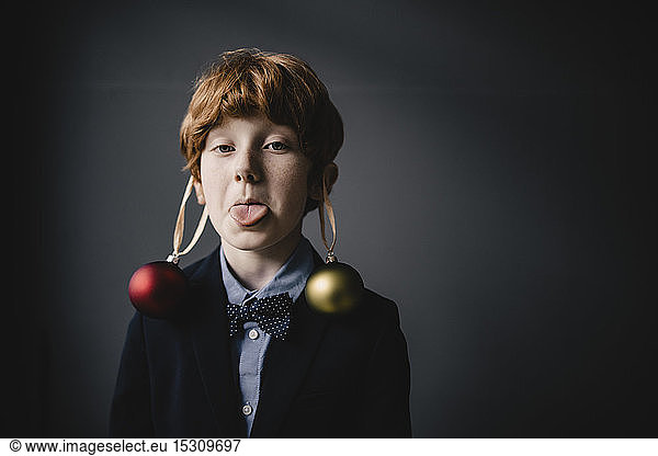 Portrait of redheaded boy wearing bow tie and Christmas baubles sticking out tongue