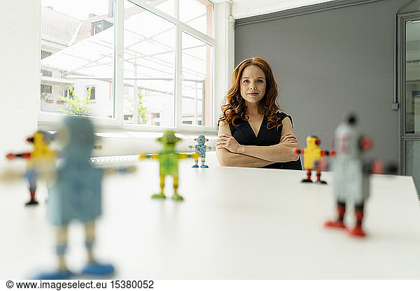 Portrait of redheaded businesswoman in a loft with miniature robots on desk