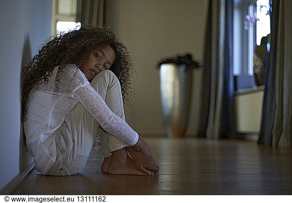 Portrait of sad girl sitting on floor at home