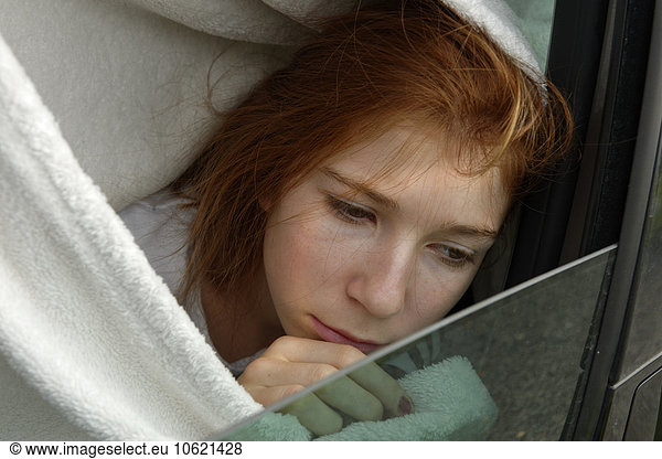 Portrait of sad redheaded girl looking through car window