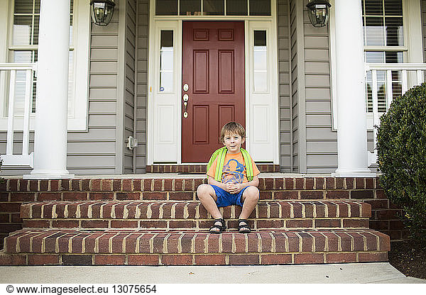 Portrait of schoolboy sitting on steps in front of house