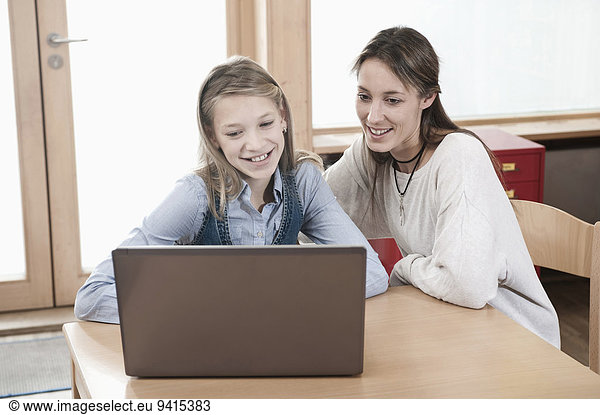 Portrait of schoolgirl and female childcare assistant looking at laptop