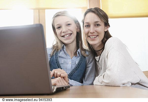 Portrait of schoolgirl and female childcare assistant with laptop