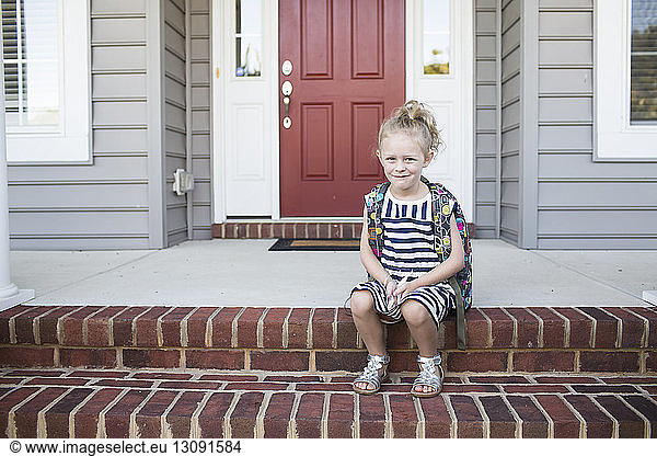 Portrait of schoolgirl sitting on steps in front of house