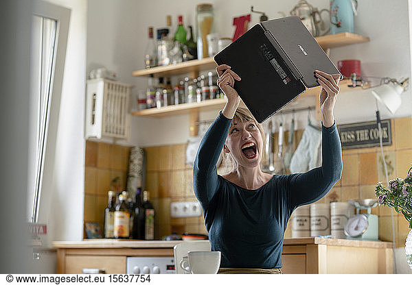 Portrait of screaming woman with laptop in the kitchen