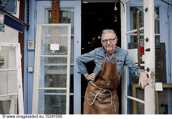 Portrait of senior hardware store owner standing with hand on hip while leaning on door