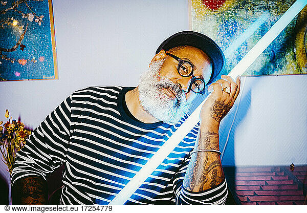 Portrait of senior hipster man with illuminated fluorescent light at apartment