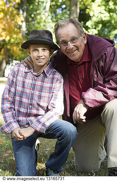 Portrait of senior man and grandson kneeling in woods