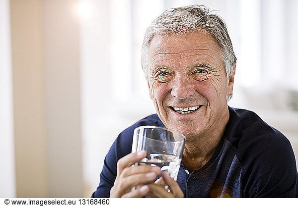 Portrait of senior man holding tumbler of water looking at camera smiling