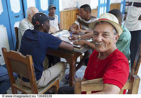 Portrait of senior man sitting with friends playing domino