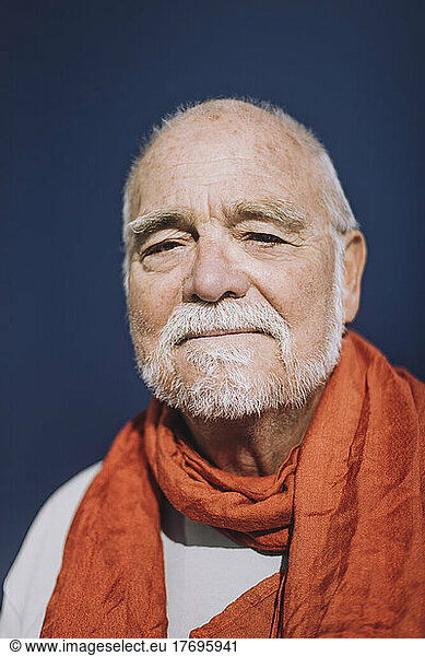Portrait of senior man wearing orange scarf against blue background