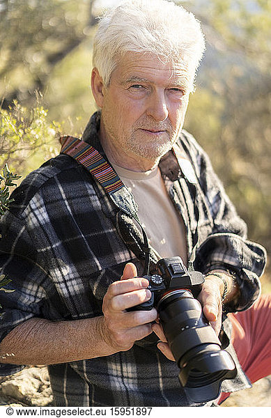 Portrait of senior man with camera in nature