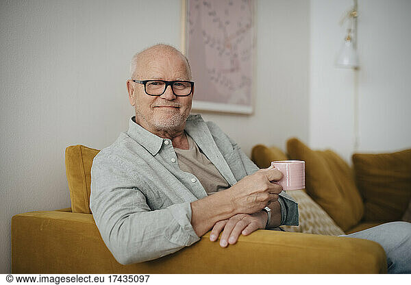 Portrait of senior man with coffee cup sitting on sofa at home