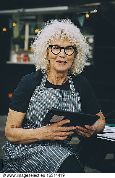Portrait of senior owner with digital tablet against food truck in city