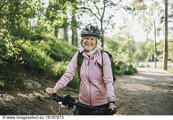 Portrait of senior woman standing with cycle on footpath