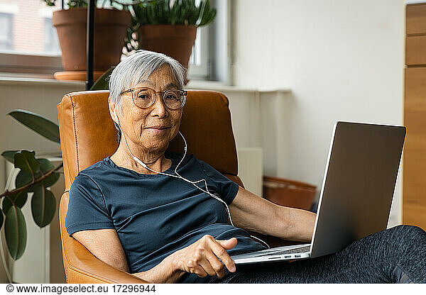 Portrait of senior woman wearing earphones while using laptop at home