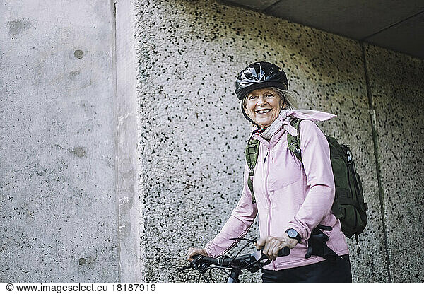 Portrait of senior woman with cycle standing near wall