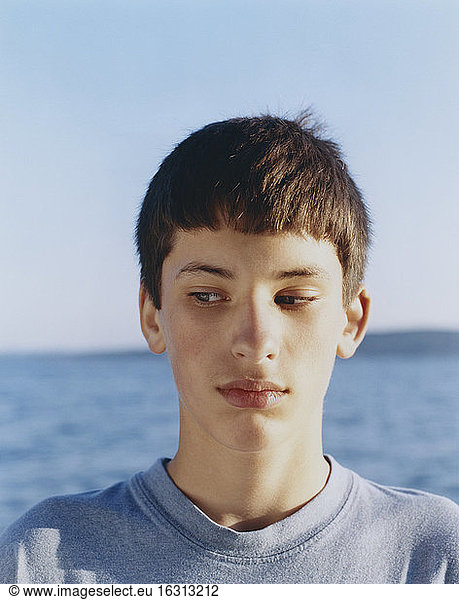 Portrait of serious adolescent boy looking away  ocean in distance