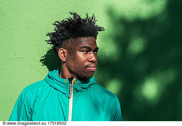 Portrait of serious black boy on green wall background.