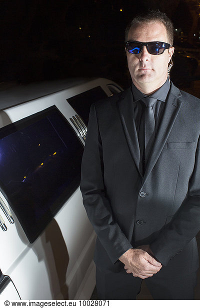 Portrait of serious bodyguard in sunglasses outside limousine at event