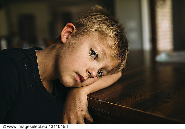 Portrait of serious boy lying head on table at home