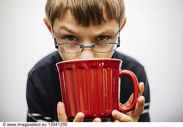 Portrait of serious boy wearing eyeglasses while holding red mug