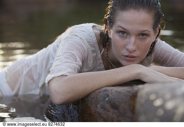 Portrait of serious woman laying on rocks in river