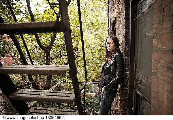 Portrait of serious woman standing at fire escape against trees