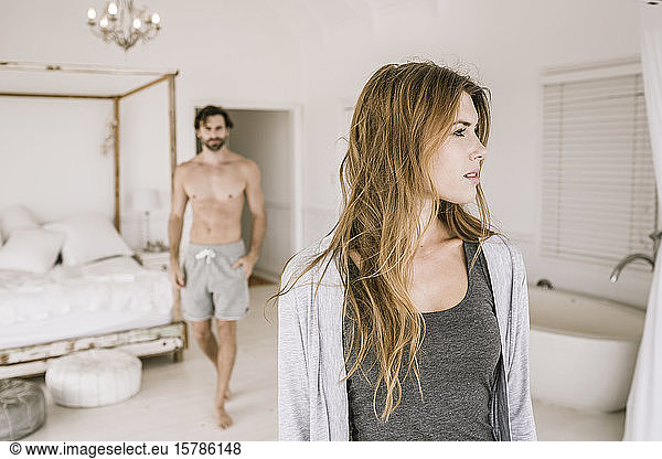 Portrait of serious young woman in bedroom with man in background