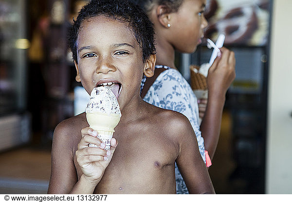 Portrait of shirtless brother licking ice cream while standing by sister